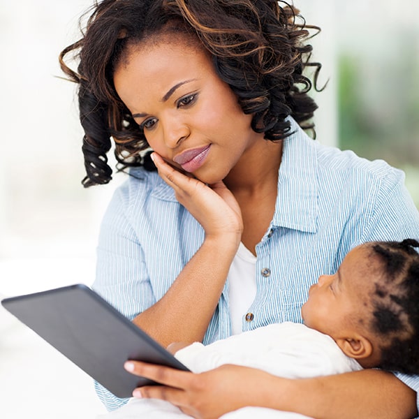 A mother reading about Orofacial Myofunctional Therapy while holding her baby